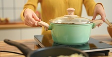 Close up shot of young woman is cooking in a green pot on a stove. People, food and domestic kitchen concept