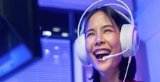 Excited young Asian girl playing online computer game with headset and microphone at home, esports and live streaming concept.