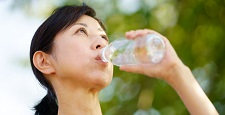 緑の中でペットボトルの水を飲む中年女性